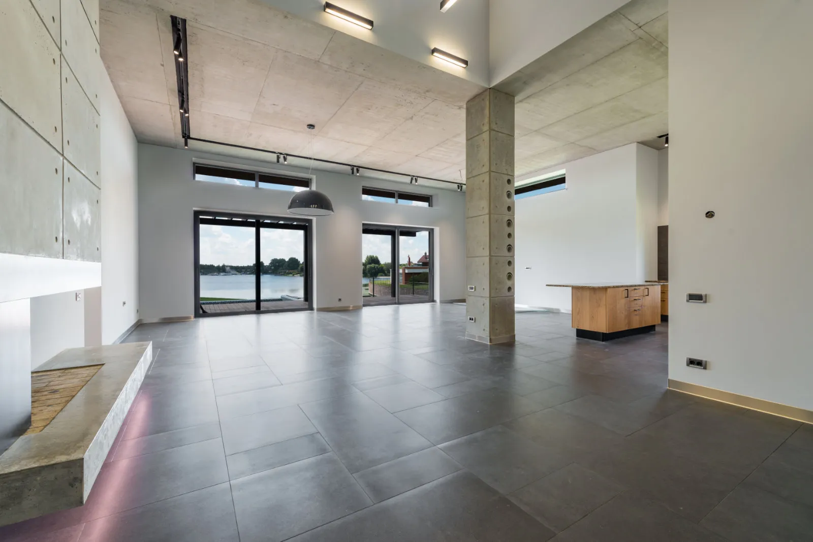 Large-format dark gray matte porcelain tiles in a modern open-concept living space with concrete ceilings