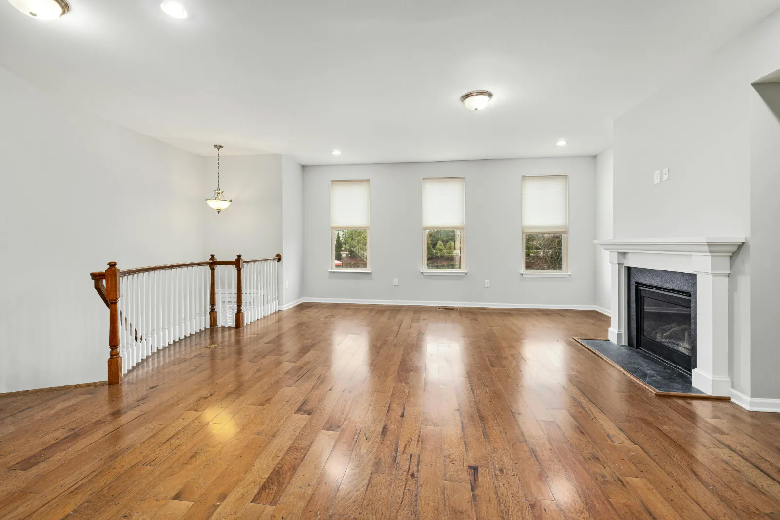Wide-plank engineered hardwood flooring in a bright open living room with fireplace and staircase